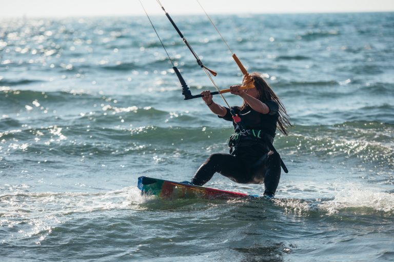 Young sporty woman on a kiteboard kitesurfing on the clear waves of the ocean and having fun. Woman kitesurfer. Active water recreational sport.